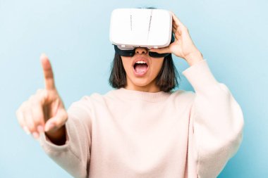 Mavi arka planda izole edilmiş sanal gözlük takan genç İspanyol kadın.