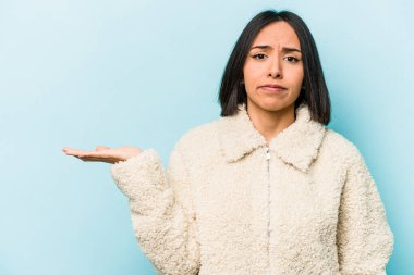 Mavi arka planda izole edilmiş genç İspanyol kadın bir avuç içinde fotokopi alanı ve belinde bir el daha gösteriyor..
