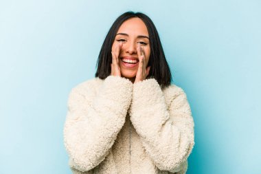 Latin kökenli genç bir kadın mavi arka planda izole edilmiş. Dedikodu yapıyor, bir şeyleri bildiriyor..