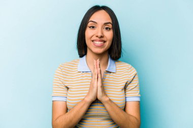 Mavi arka planda izole edilmiş genç İspanyol bir kadın el ele tutuşup ağzının kenarında dua ediyor, kendinden emin hissediyor..