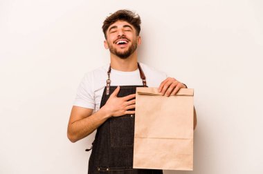 Beyaz arka planda izole edilmiş bir çanta taşıyan genç İspanyol tezgahtar elini göğsünde tutarak kahkahalar atıyor..