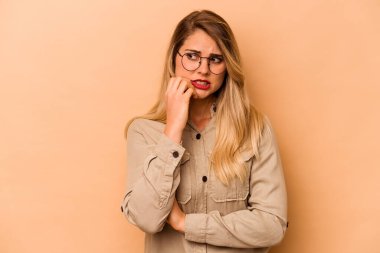 Beyaz tenli genç bir kadın bej arka planda izole edilmiş tırnak yiyor, gergin ve çok endişeli..