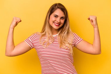 Sarı arka planda izole edilmiş genç beyaz kadın güçlü bir hareket sergiliyor, kadınsı gücün sembolü.