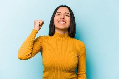 Mavi arka planda izole edilmiş genç İspanyol kadın zaferi, tutkuyu ve coşkuyu, mutlu ifadeyi kutluyor..