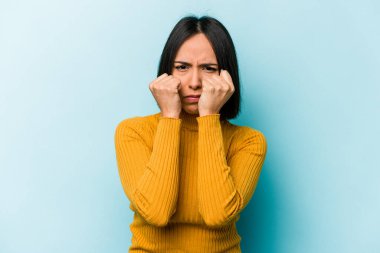 Mavi arka planda izole edilmiş genç İspanyol kadın bir tartışma yüzünden yumruk atıyor, sinirleniyor, kavga ediyor..