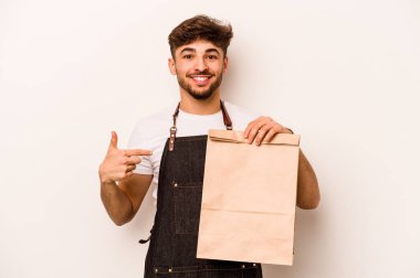 Beyaz arka planda izole edilmiş bir çanta taşıyan genç İspanyol tezgahtar gömlek fotokopi alanını işaret ediyor, gururlu ve kendinden emin.