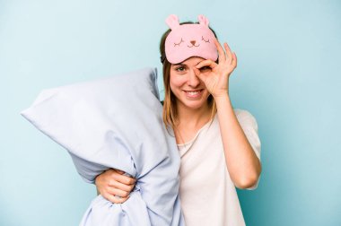 Mavi arka planda izole edilmiş pijama giyen beyaz bir kadın heyecanlı..