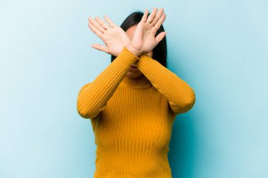 Mavi arka planda izole edilmiş genç İspanyol kadın iki kolu çapraz tutuyor, inkar kavramı.