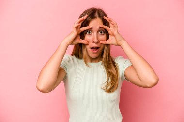 Pembe arka planda izole edilmiş genç beyaz kadın bir başarı fırsatı bulmak için gözlerini açık tutuyor..