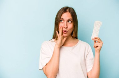 Mavi arka planda izole edilmiş hijyenik peçete tutan beyaz bir kadın gizli sıcak fren haberini veriyor ve kenara bakıyor.