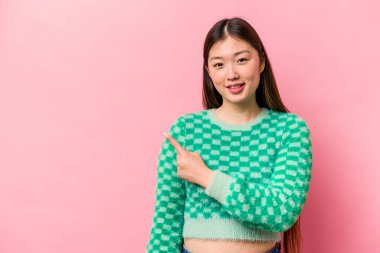 Pembe arka planda izole edilmiş genç bir Çinli kadın gülümsüyor ve boş alanda bir şeyler gösteriyor..