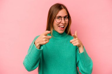 Pembe arka planda izole edilmiş genç beyaz kadın parmaklarıyla ön tarafı işaret ediyor..