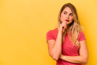 Sarı arka planda izole edilmiş genç beyaz kadın rahatça fotokopi odasına bakan bir şey düşünüyor..