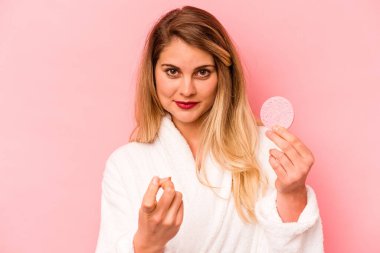 Pembe arka planda yüz süngeri tutan genç beyaz kadın seni işaret ediyor sanki davet ediyormuş gibi..