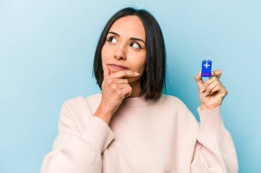 Mavi arka planda pil tutan genç İspanyol kadın şüpheli ve şüpheci bir ifadeyle yana bakıyor..