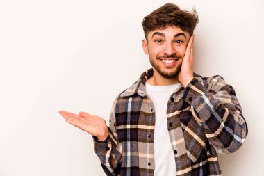 Beyaz arka planda izole edilmiş genç İspanyol bir adam avuç içinde fotokopi alanı tutuyor, el üstünde tutuyor. Şaşırmış ve mutlu..