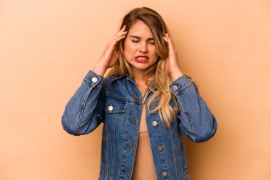 Beyaz tenli genç bir kadın bej arka planda izole edilmiş tapınaklara dokunuyor ve baş ağrısı çekiyor..