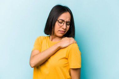 Mavi arka planda izole edilmiş genç İspanyol kadın omuz ağrısı çekiyor..
