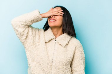 Mavi arka planda izole edilmiş genç İspanyol kadın mutlu bir şekilde ellerini başının üstünde tutarak gülüyor. Mutluluk kavramı.