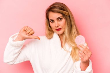 Pembe arka planda yüz süngeri tutan genç beyaz kadın gururlu ve kendinden emin hissediyor, örnek olarak..