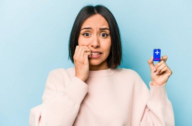 Mavi arka planda pil tutan genç İspanyol kadın tırnaklarını yiyor, gergin ve çok endişeli..