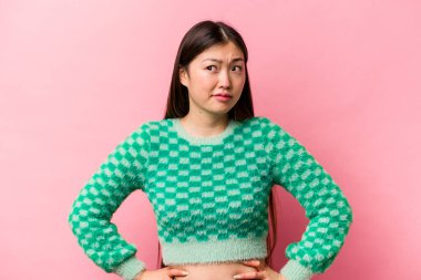 Pembe arka planda izole edilmiş genç Çinli kadın kafası karışmış, şüpheli ve güvensiz hissediyor..