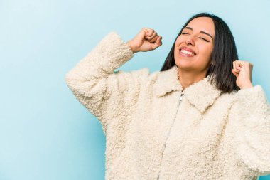 Genç İspanyol kadın mavi arka planda izole edilmiş zafer sonrası yumruğunu kaldırıyor, kazanan konsept..