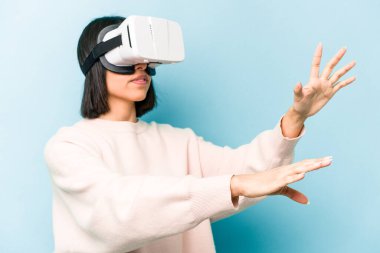 Mavi arka planda izole edilmiş sanal gözlük takan genç İspanyol kadın.