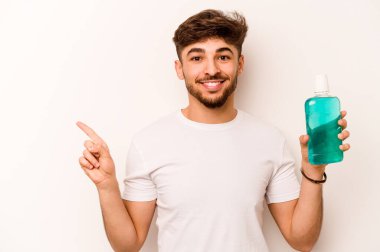 Beyaz arka planda izole edilmiş ağız gargarası tutan genç İspanyol adam gülümsüyor ve boş alanda bir şeyler gösteriyor..