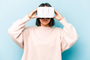 Mavi arka planda izole edilmiş sanal gözlük takan genç İspanyol kadın.