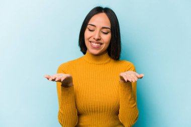 Mavi arka planda izole edilmiş genç İspanyol kadın elinde avuç içi bir şeyle kameraya sunuyor..