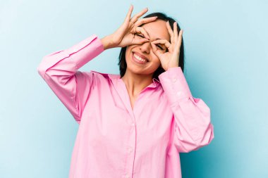 Mavi arka planda izole edilmiş genç İspanyol kadın gözlerinde sorun olmadığını gösteriyor.