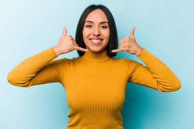 Mavi arka planda izole edilmiş genç İspanyol kadın parmaklarıyla bir cep telefonu hareketi gösteriyor..