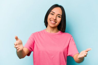 Mavi arka planda izole edilmiş genç İspanyol kadın hoş bir yüz ifadesi sergiliyor..