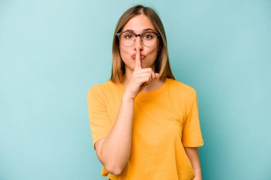Mavi arka planda izole edilmiş genç beyaz kadın ya sır saklıyor ya da sessizlik istiyor..