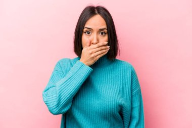 Pembe arka planda izole edilmiş genç İspanyol kadın elleri endişeli bir şekilde ağzı örtüyor..