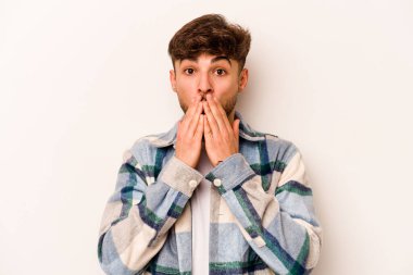 Beyaz arka planda izole edilmiş genç İspanyol adam elleriyle ağzını kapatırken şok oldu..