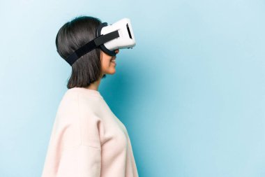 Mavi arka planda izole edilmiş sanal gözlük takan genç İspanyol kadın.