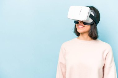 Mavi arka planda izole edilmiş sanal gözlük takan genç İspanyol kadın.