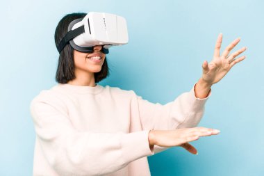 Mavi arka planda izole edilmiş sanal gözlük takan genç İspanyol kadın.