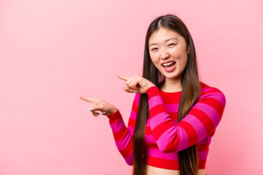 Pembe arka planda izole edilmiş genç bir Çinli kadın işaret parmağıyla işaret ederek heyecanlanıyor..