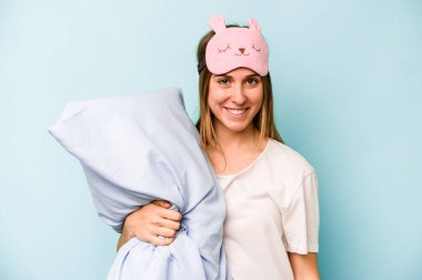 Mavi arka planda izole edilmiş pijama giyen genç beyaz kadın mutlu, güler yüzlü ve neşeli..