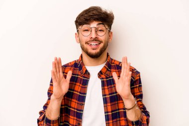 Beyaz arka planda izole edilmiş genç İspanyol adam yüksek sesle gülüyor elini göğsüne koyuyor..