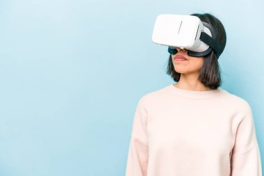 Mavi arka planda izole edilmiş sanal gözlük takan genç İspanyol kadın.