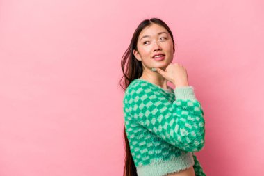 Genç Çinli kadın pembe arka planda izole edilmiş, başparmak uzakta, gülüyor ve kaygısız..