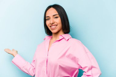 Mavi arka planda izole edilmiş genç İspanyol kadın hoş bir yüz ifadesi sergiliyor..