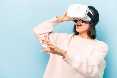 Mavi arka planda izole edilmiş sanal gözlük takan genç İspanyol kadın.