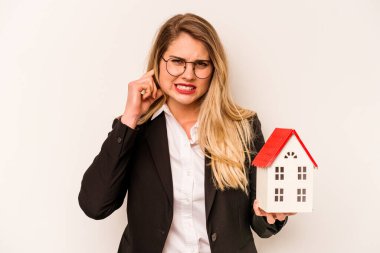 Beyaz arka planda izole edilmiş, elleri kulaklarında oyuncak evi tutan beyaz bir kadın..