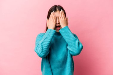 Pembe arka planda izole edilmiş genç Çinli kadın yüzünün yarısını avuç içiyle kaplayarak eğleniyor..
