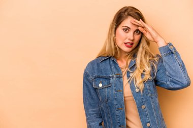 Beyazlı genç bir kadın bej arka planda izole edilmiş, uzaklara bakıyor ve elini alnına koyuyor..